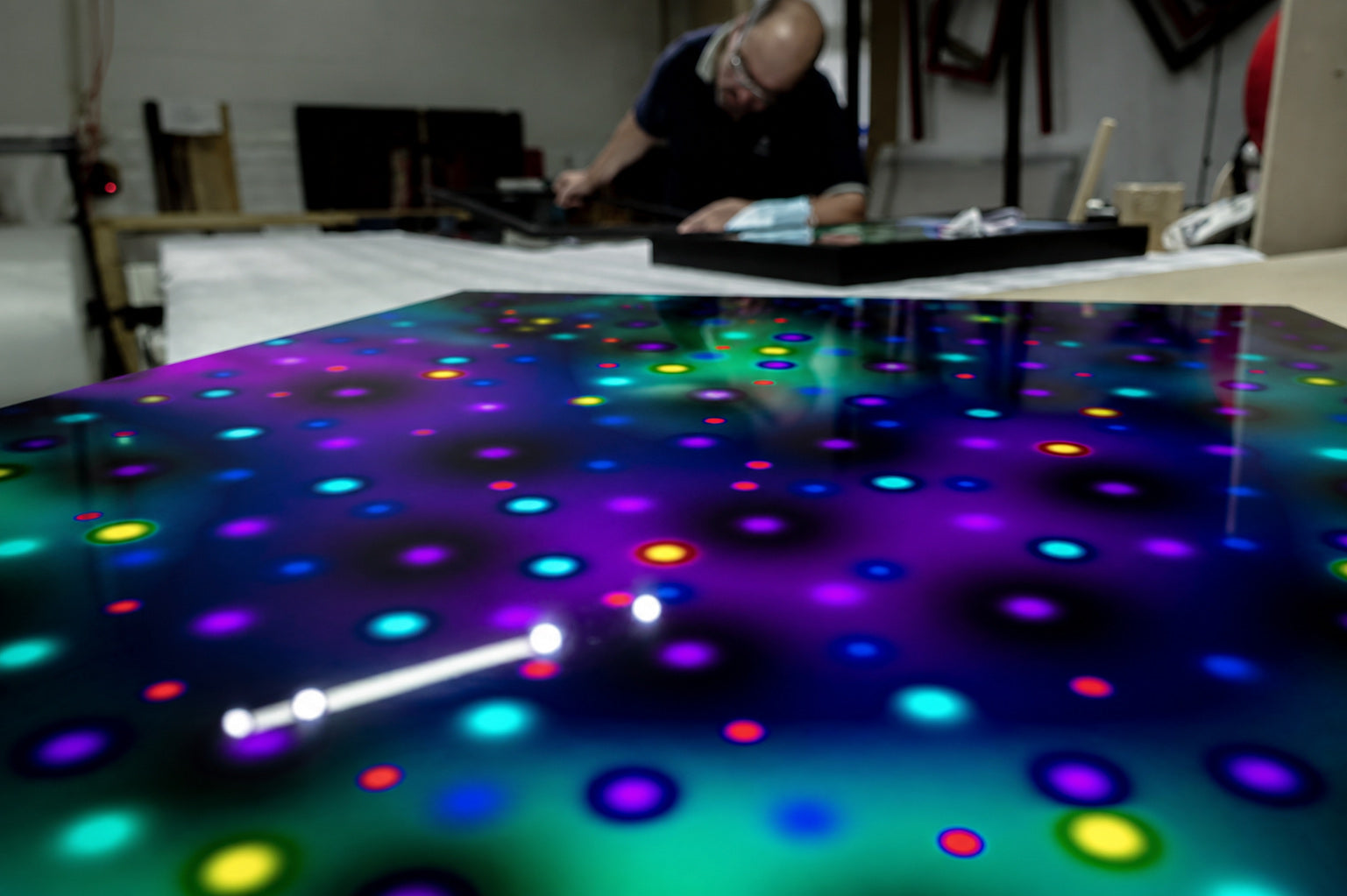 Un technicien de l’atelier assemble une pièce encadrée à l’établi, derrière une grande image imprimée